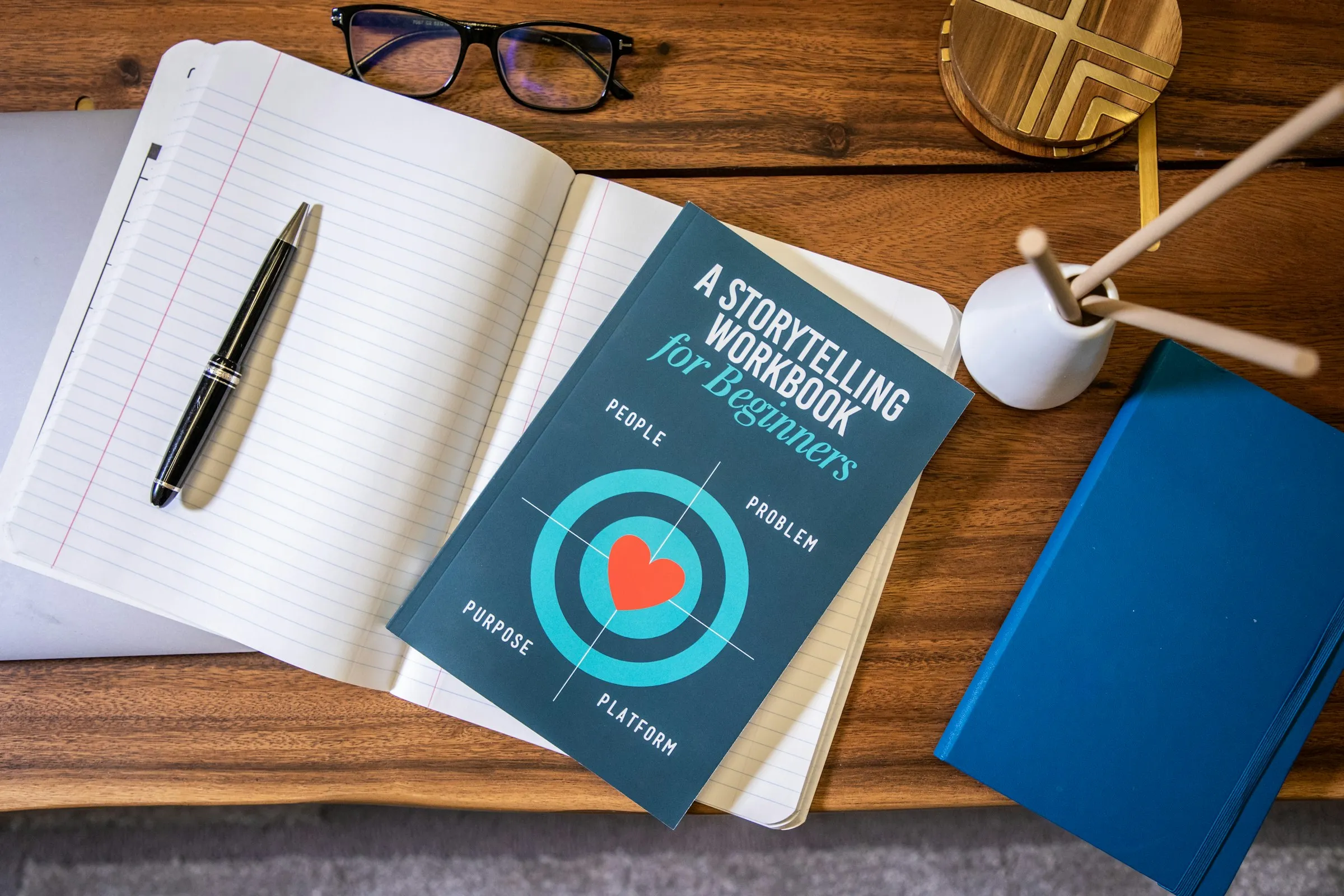 A storytelling workbook on a desk beside a pen and notebooks